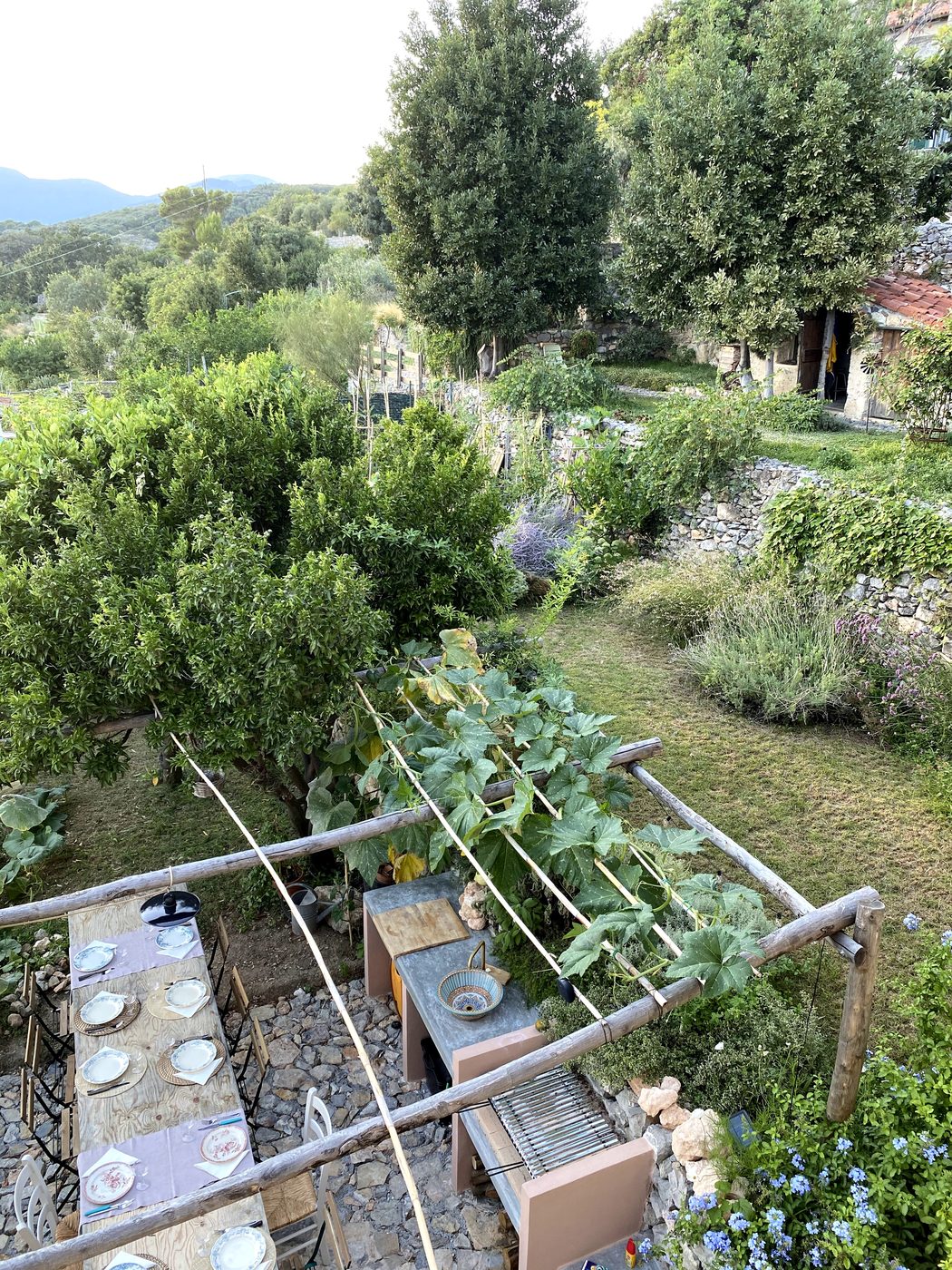 Private garden at Ca' Remurin, Verezzi, with an outdoor dining table set under a wooden pergola among climbing vines
