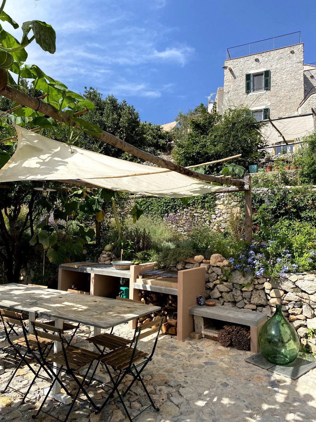 Garden corner at Ca' Remurin with dry-stone wall, wildflowers and a glimpse of the Verezzi hillside, Liguria